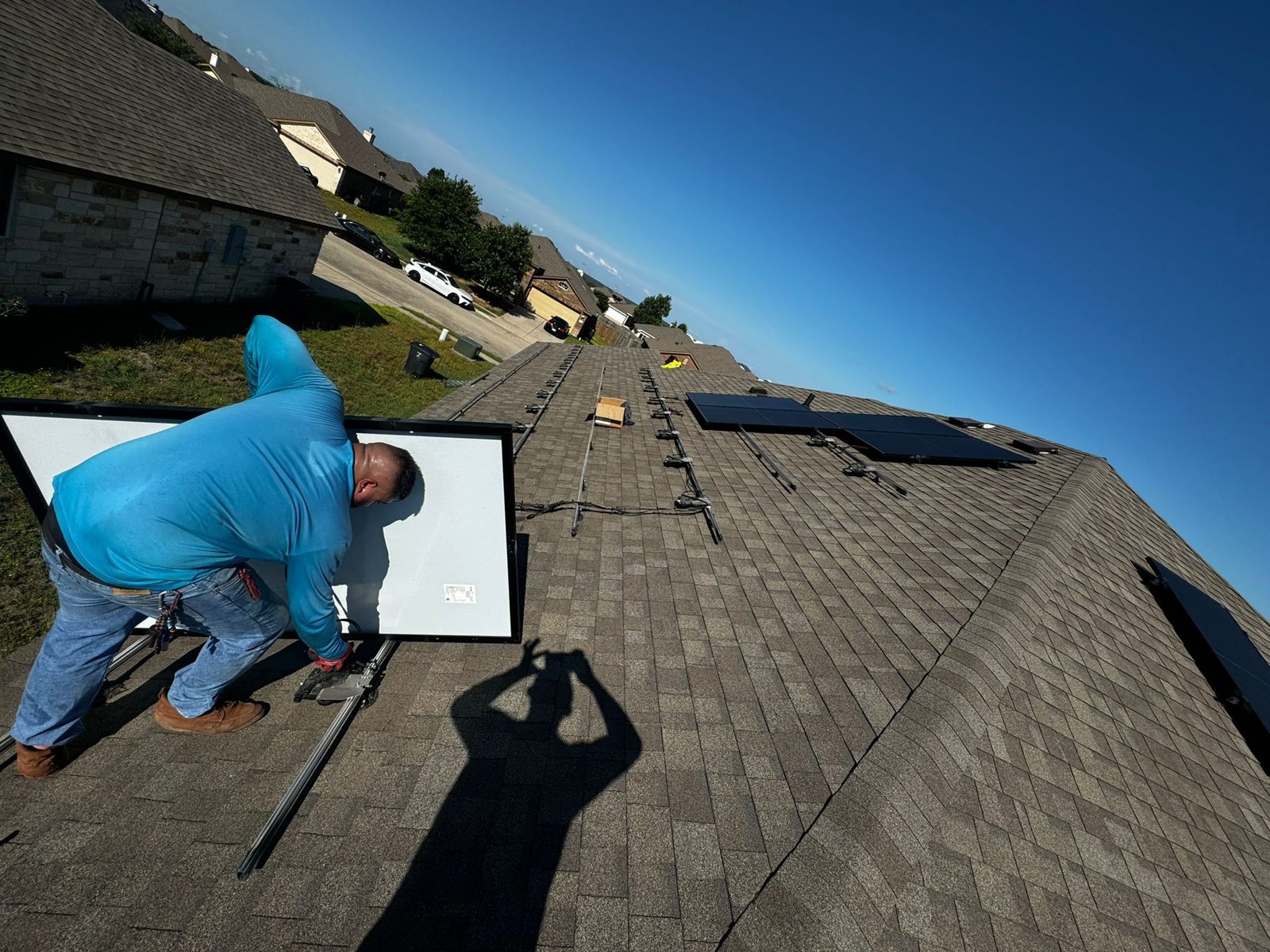 Crew member setting a solar panel on a shingle roof, military veteran solar project